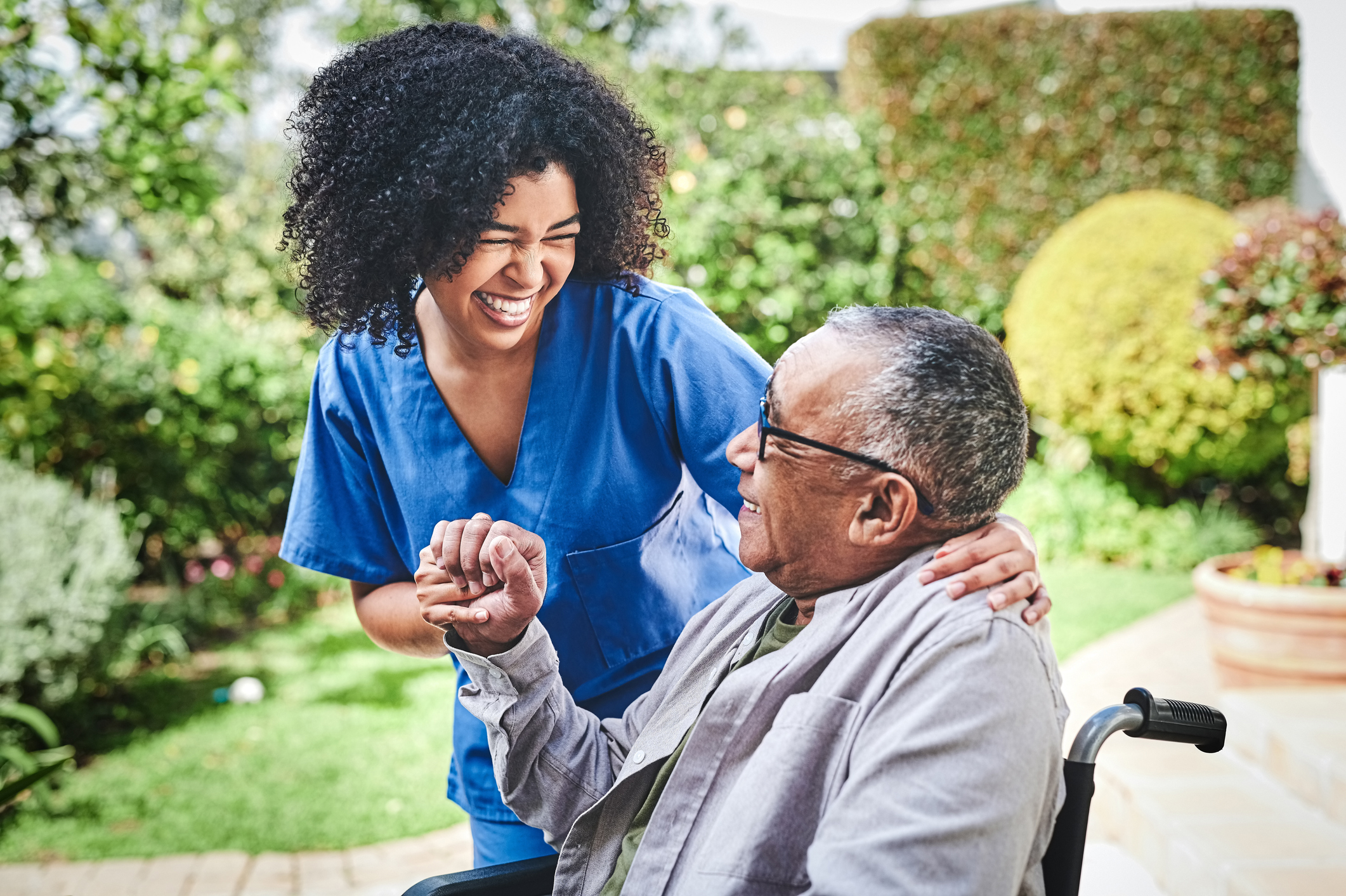 Patient in a wheelchair and nurse standing beside him holding hands and smiling at one another