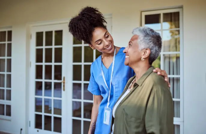 A nurse stands with her arm wrapped around a patient as they smile at each other